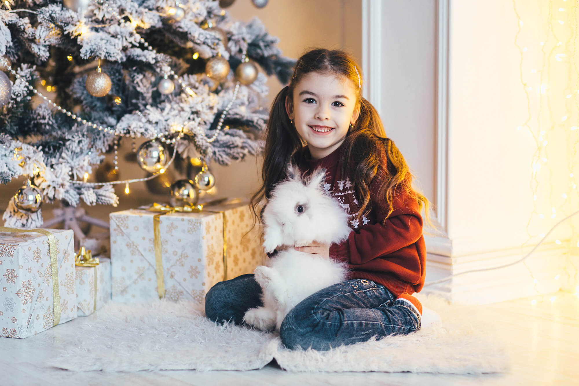 Niña con conejo al lado del árbol de Navidad y regalos